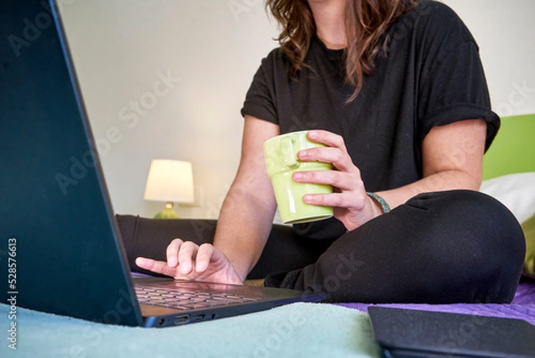 Fototapeta Female working from home by a laptop with a mug in a hand