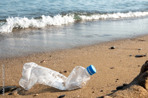 Fototapeta Spilled garbage on the beach of the big city. Empty used dirty plastic bottles. Dirty sea sandy shore the Black Sea. Environmental pollution. Ecological problem. Bokeh moving waves in the background