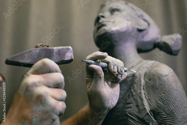 Fototapeta Man sculptor creates sculpt bust human woman sculpture with hammer. Statue craft creation workshop.