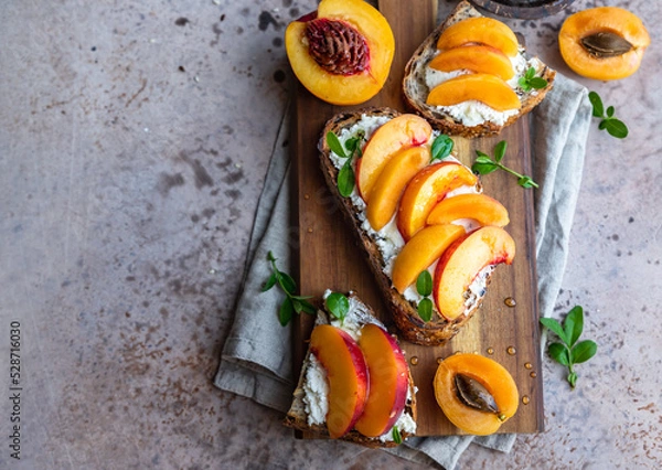 Obraz Open sandwiches with tartine bread and cream cheese, nectarine and apricot drizzled with honey on wooden cutting board. Top view.