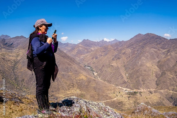 Obraz Elderly Caucasian woman calling on a cell phone on top of a mountain.
