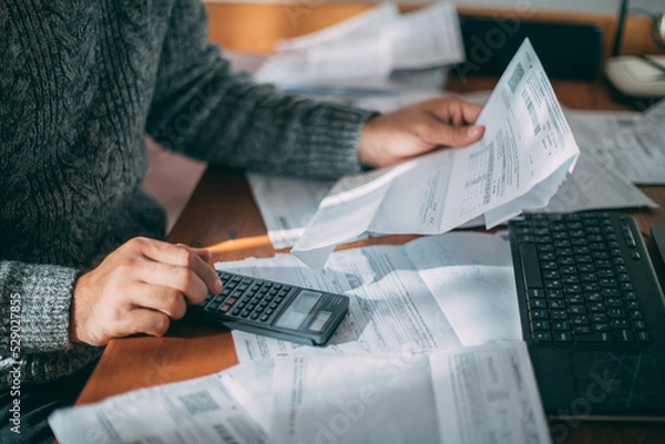 Fototapeta Close-up of male hands with a utility bill, a lot of checks and a calculator on the table.