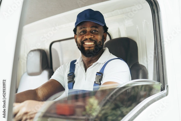 Fototapeta Portrait of courier black man in the truck thumb up and smiling to camera while sitting in driver seat, Optimistic man worker with delivery occupation.