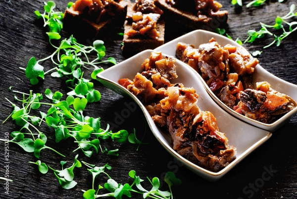 Fototapeta Appetizer of fried eggplant with prunes in unusual plates, a lot of microgreens scattered around, on a black textured background, delicious food