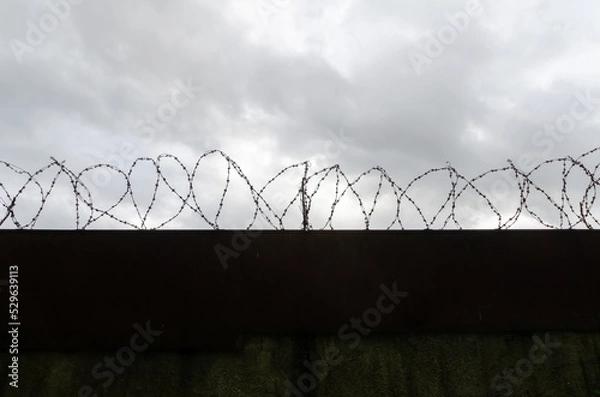 Obraz fence barbed wire gray sky clouds danger zone safety passage closed hopelessness decay