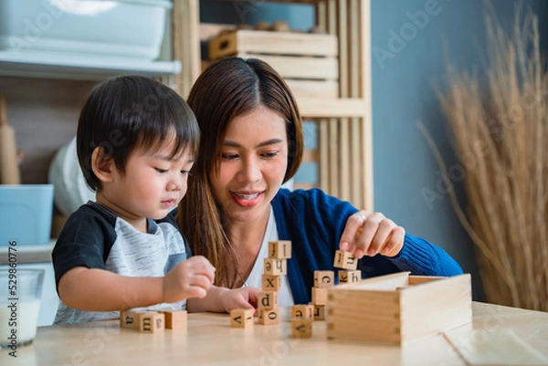 Obraz Mother is teaching her cute little son to play with toys in the kitchen.