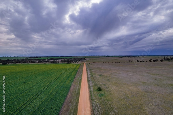 Obraz Looking down on a dirt road in a country setting with storm clouds on the horizon.