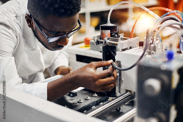 Obraz African engineer programming equipment with tablet at factory