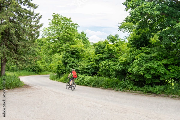 Obraz A man quickly rides a bicycle against the backdrop of a green forest