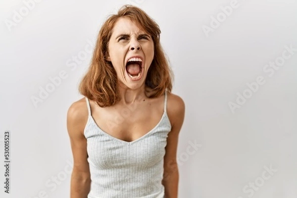 Fototapeta Beautiful caucasian woman standing over isolated background angry and mad screaming frustrated and furious, shouting with anger. rage and aggressive concept.