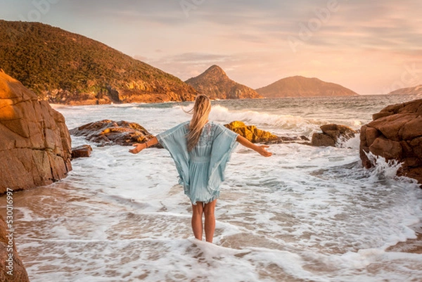 Obraz Woman stands in ocean wabes with a soft pastel sunrise sky