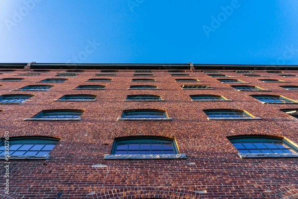 Fototapeta The wall of the historical building of the cotton factory with the clock tower in the old industrial park on the river Nashua, View from the bottom up
