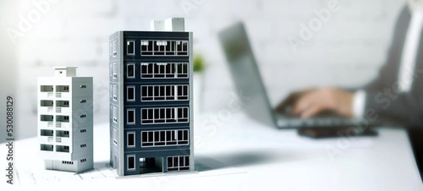 Fototapeta property management, real estate business, housing development. businessman working on laptop in office with building models on table. banner with copy space