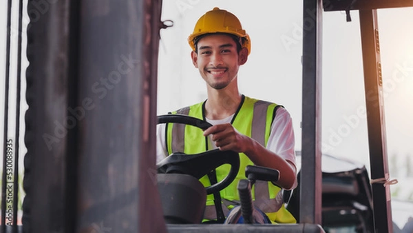 Fototapeta Young Asian work man driving the truck over construction site. Industrial factory worker operating on forklift in the import export shipyard. Foreman at warehouse logistic in Cargo freight ship.