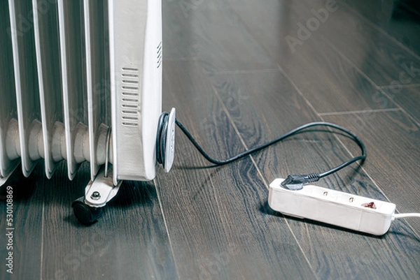 Obraz oil electric heater on a wooden floor is plugged into a socket. Building space heating