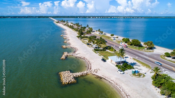 Fototapeta Aerial Drone Close Up of the Causeway Bridge in Sanibel, Florida with the Bay and a Preserve in the Foreground and the Gulf of Mexico in the Background Featuring a Blue Sky and Blue Water