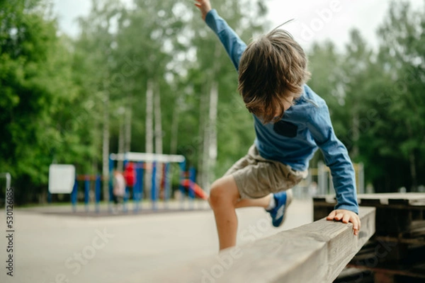 Fototapeta A five-year-old boy parkours in the park in the summer, the child jumps over a high barrier