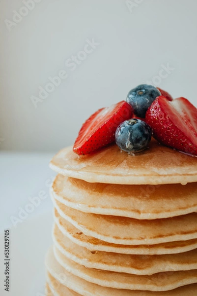 Fototapeta Pancakes with maple syrup, strawberry, and blueberries in a plate close-up. Sweet tasty breakfast, dessert. American pancakes with berries.