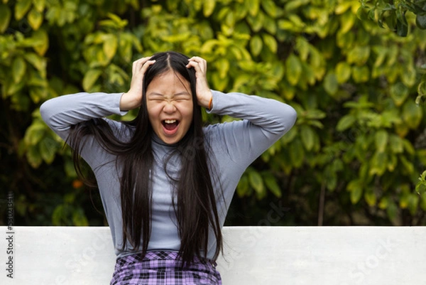 Fototapeta An Asia girl is screaming with 2 hands touching her head in natural light.