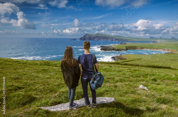 Obraz Young man and woman (couple) thoughtfully look at the sea landscape of Coumeenoole beach at the Atlantic coast of Ireland, Wild Atlantic Way Tour, Ireland