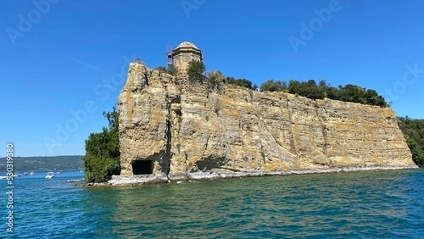 Fototapeta island in the Bolsena lake on a sunny summer day in the Lazio region of Italy with blue sky and rocky cliff