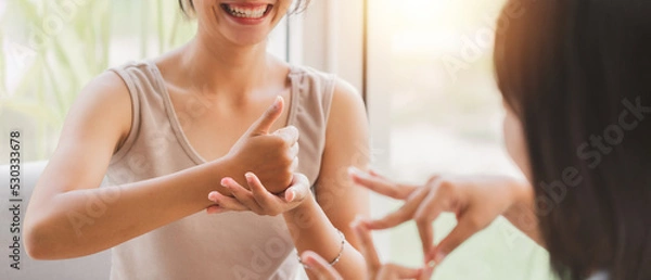 Obraz Young attractive Asian women using sign hand finger language conversation with deaf person. Cheerful happy using nonverbal communication to persons with disabilities.