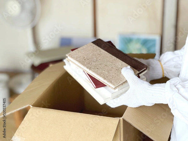 Fototapeta ダンボール箱に本などを入れる軍手をした手と散らかった部屋