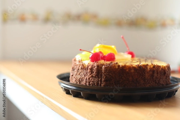 Obraz Closeup view of fruits cake on sunny home background. Beautiful delicious bakery. Sweet dessert close-up. Macro. Cherry and chocolate sweets. Birthday party with family. 
