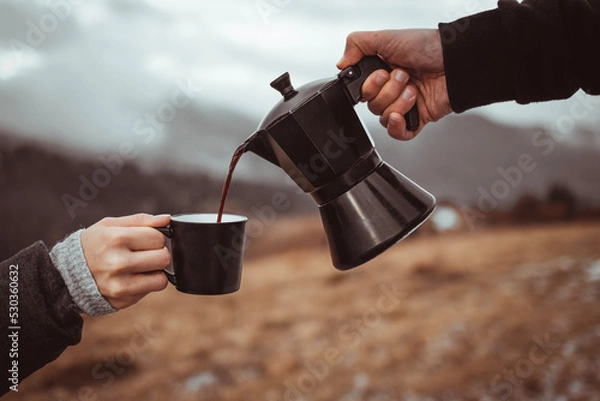 Fototapeta Person pouring out coffee from moka pot into cup outdoors with fog background
