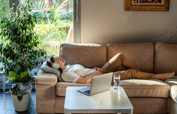 Fototapeta Young woman having online hypnotherapy regression session with psychotherapist lying on sofa at home. Digital service