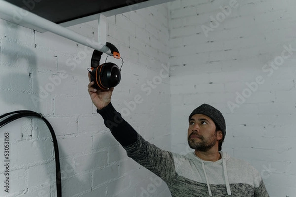 Fototapeta Man in a cap hanging wireless helmets on a pipe