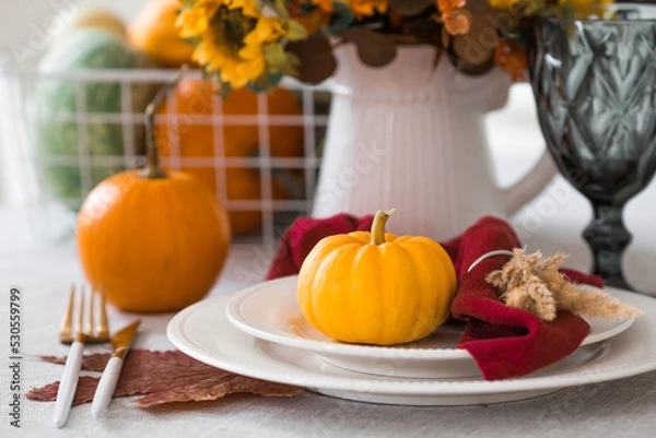 Obraz Beautiful autumn table setting. A plate with a cotton napkin and pumpkins. Table gold and a vase with autumn flowers on a linen tablecloth. The concept of festive serving for Thanksgiving.