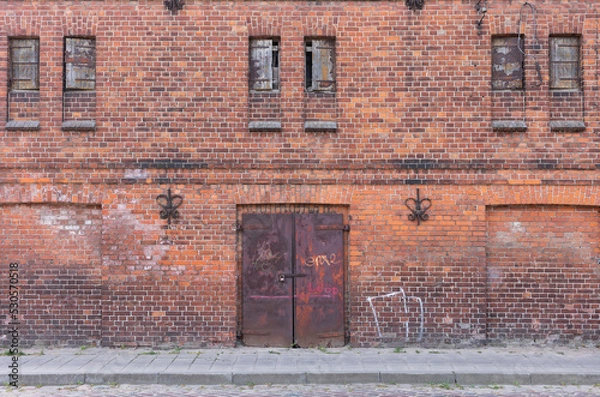 Obraz Wall of an old red brick factory building with narrow windows and metal gates