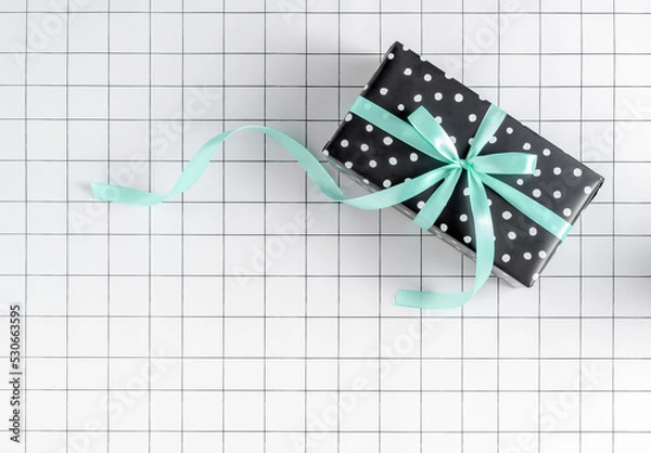 Fototapeta New Year giveaway wrapping paper gift box with green ribbon bow on grid background. Christmas celebration, birthday suprise present aesthetic. Shopping, party minimal concept. Copy space.