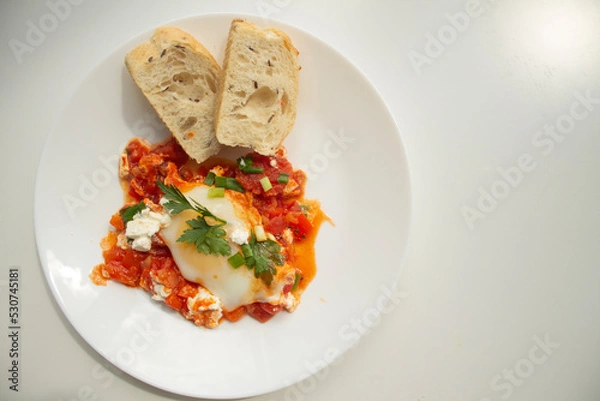 Fototapeta Traditional shakshuka with eggs, tomato, and parsley on white background