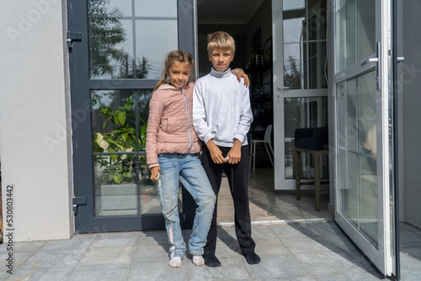 Fototapeta Two happy siblings having fun together standing on terrace. Adorable brother and sister hugging and looking at camera on porch of their house