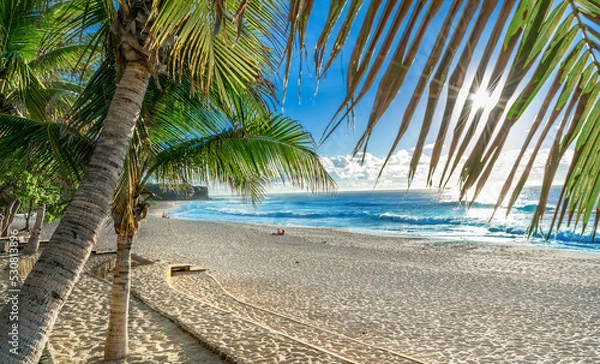 Fototapeta Wide view of the sunrise in Boucan Canot beach in the summertime, with blue sea water and yellow sand in Reunion