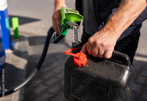 Fototapeta A man fills fuel in a plastic can at a gas station