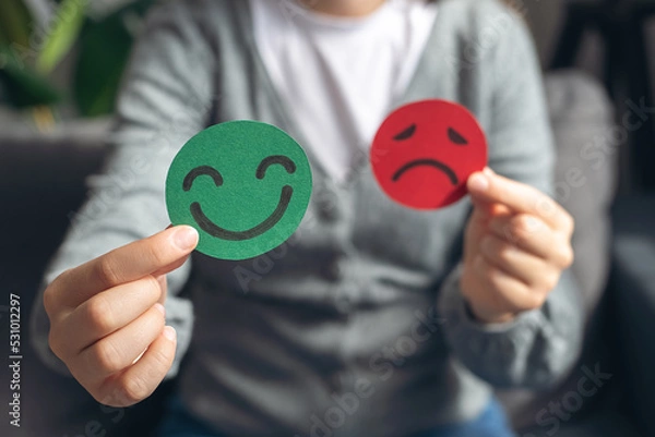Obraz Selective focus of female hands holding happy and angry face paper sit on sofa. Feedback rating, emotional intelligence, balance emotion control, mental health assessment, bipolar disorder concept