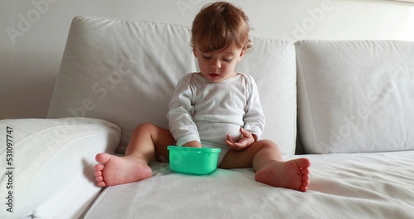 Fototapeta Baby eating afternoon snack on couch. Calm one year old toddler boy resting on sofa