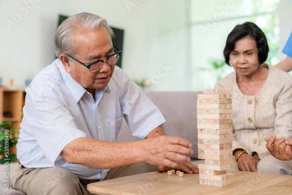 Obraz Dementia therapy in playful way. Group of senior elder people stay at nursing home, enjoy activity.relation playing Jenga or tumbling tower wood block game. Training fingers and fine skills