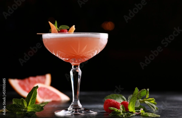 Fototapeta Drinks and cocktails. A light red drink with grapefruit, raspberries, mint and ice in a glass on a black table. Bar menu. Background image, copy space