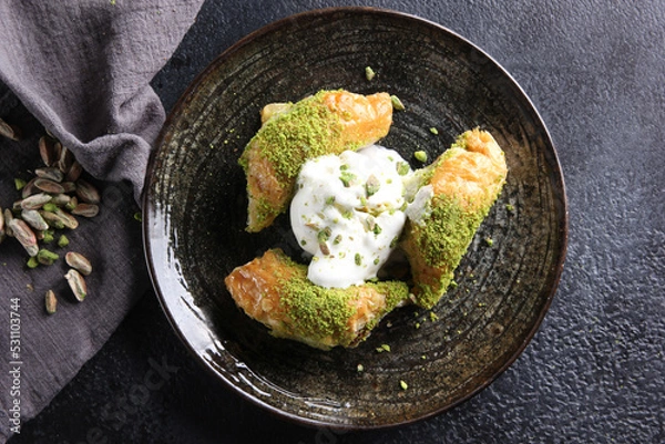 Fototapeta Oriental sweets. Pahlava with ice cream nuts, pistachio in a large dish on a black table. Turkish dessert. Background image, copy space, horizontal