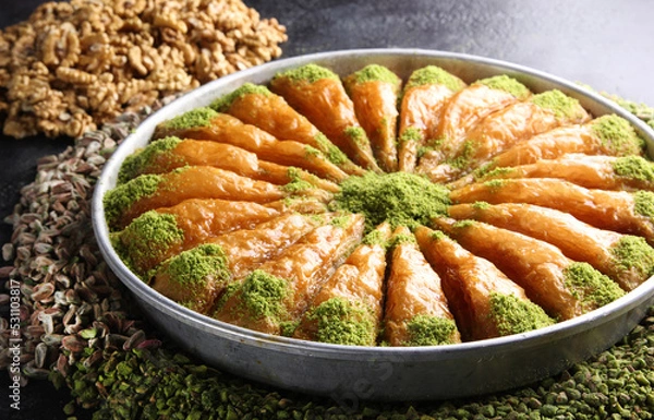 Fototapeta Oriental sweets. Pahlava with nuts, pistachio in a large dish on a black table. Turkish dessert. Background image, copy space, horizontal, top view, flatlay