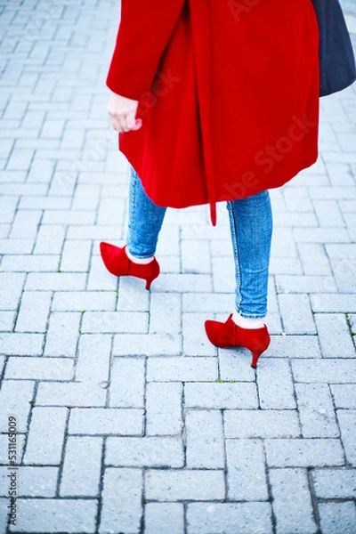 Fototapeta Middle-aged woman walking to a job interview dressed in blue jeans and red coat looking to the side. Cobblestone background. Copy space Business executive woman.