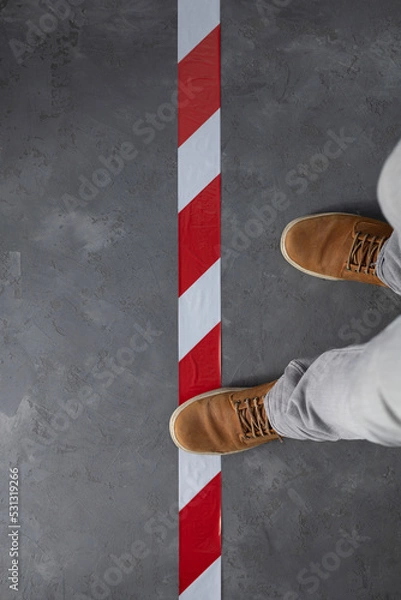 Fototapeta Man step over barrier tape and old boots shoes at cement floor background. Signal warning tape