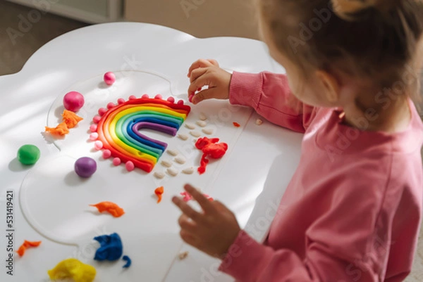 Fototapeta A little girl playing with rainbow from play dough for modeling. Art Activity for Kids. Fine motor skills. Sensory play for toddlers..