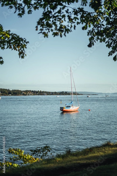 Fototapeta kleines rotes segelboot ankert auf dem wasser in der abendsonne in Norwegen