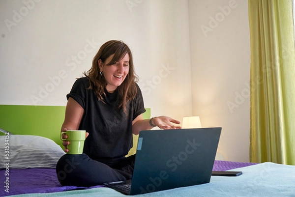 Fototapeta Woman sitting on the bed and working with a computer