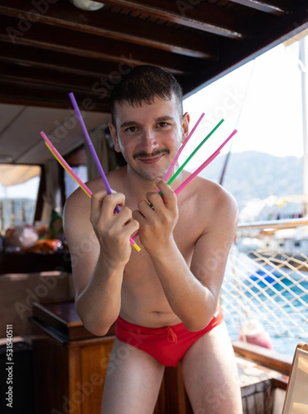 Fototapeta Handsome young man wearing speedo dancing. Holding colorful drinking straws on his hand. Straws are like Wolverine's claws. Enjoy, fun, holiday and summer concept.